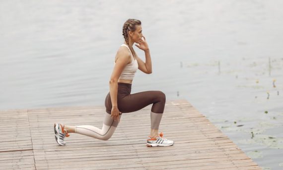 A woman performs lunges on a lakeside wooden deck, showcasing a fit lifestyle outdoors.