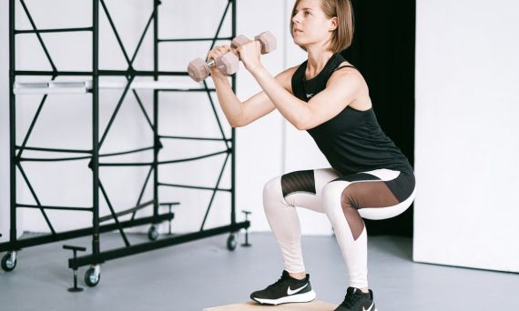 A woman in sportswear performs a squat with dumbbells indoors, embodying strength and healthy living.
